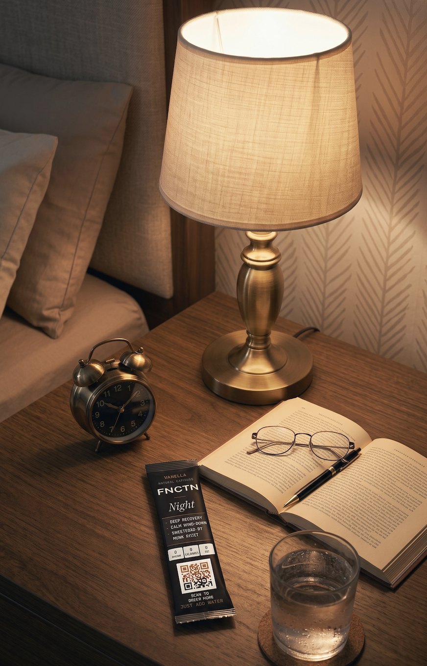 A FNCTN NIGHT stick on a bedside table beside a book and a glass of water
